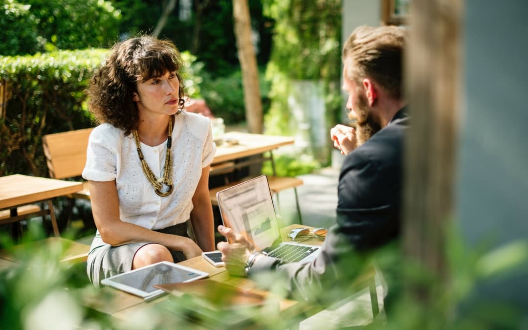 a woman and a man talking about online travel deals, sitting outside on the terrace in the sun